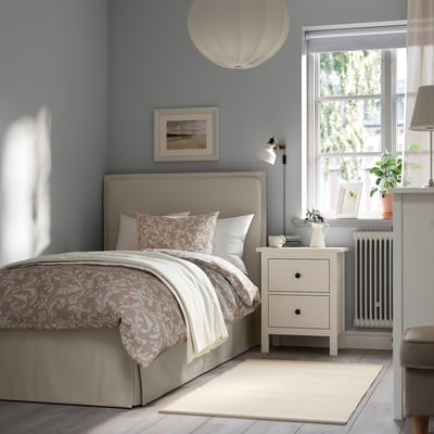 Serene bedroom: TÄRNKULLEN bed in beige, with a soft headboard, patterned bedding, and a nightstand with a lamp. Large window with soft light.