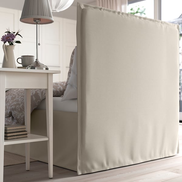 Bed with soft, padded headboard and removable, washable cover. Lamp and decorative items on bedside table.