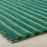 Striped wool rug with varied shades of green, texture detailed, laid on wooden floor.