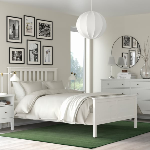 Small green TIDTABELL rug under white bed, contrasting with larger photos and furniture.
