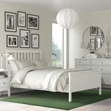 Small green TIDTABELL rug under white bed, contrasting with larger photos and furniture.