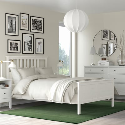 Small green TIDTABELL rug under white bed, contrasting with larger photos and furniture.