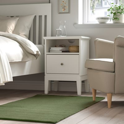Modern bedroom: TIDTABELL nightstand, bed with gray linens, green rug, upholstered chair.