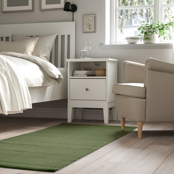 Bedroom with TIDTABELL green rug, white bed, nightstand, and striped chair by window.