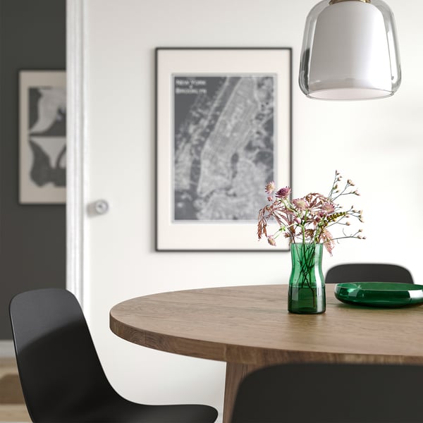 Modern dining table with black chair, TIDVATTEN green vase of dried flowers, hanging light, and wall map.