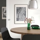 Modern dining table with black chair, TIDVATTEN green vase of dried flowers, hanging light, and wall map.
