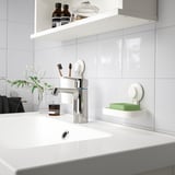 Modern white bathroom sink with chrome faucet. Small TISKEN green soap dish, toothbrush holder, and plant. Clean, minimalist design.