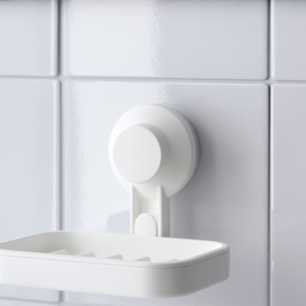 A white soap dish securely attached to a tiled wall using a strong suction cup. The dish is simple and modern, with drainage slots to keep it dry.