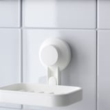 A white soap dish securely attached to a tiled wall using a strong suction cup. The dish is simple and modern, with drainage slots to keep it dry.