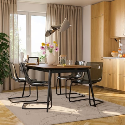 Modern dining area with walnut extendable table, black chairs, and flowers. Kitchen with window and plant.