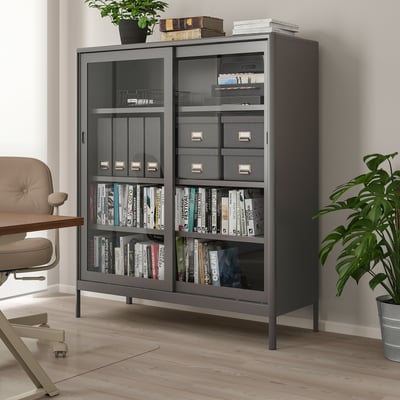 Black TJOG magazine file made of recycled materials, organized in a room with chair, plant, and bookcase.