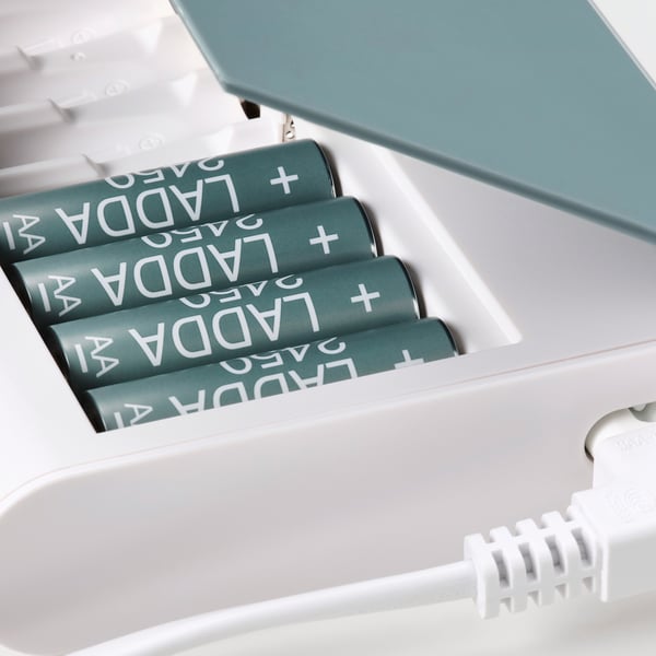 Four green rechargeable batteries labeled ladda in an open white charger with a clear lid.