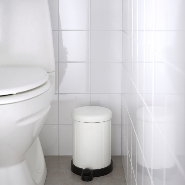 White bathroom trash can with a foot pedal for hands-free use, positioned next to a toilet.