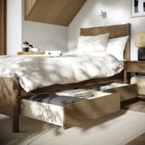 Bedroom with wooden bed, white linens, and open drawer underneath. Coffee items on bedside tray.