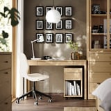 Modern home office with TONSTAD oak desk, white chair, photos, and globe lamp. Natural light fills the room.
