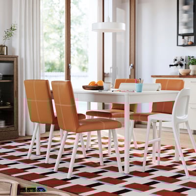 Modern dining set with orange leather chairs and white table on a colorful rug in a well-lit room.