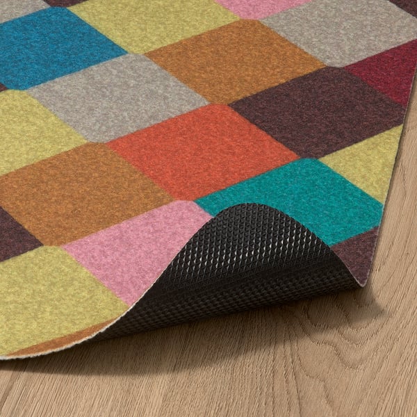 Bright, multicolored geometric rug with a textured black rubber backing, partially lifted to show quality.