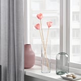 Three pink flowers in a clear glass vase on a windowsill, flanked by two decorative vases.