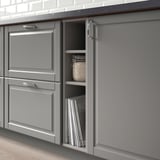 Gray kitchen cabinets display open section showing cookbooks and jar, demonstrating organized storage of kitchen items.