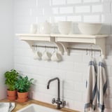 White shelf holds mugs, bowls, and pots; hooks below for hanging towels, kitchen against tiled wall.