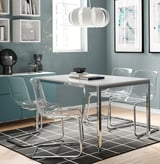 Modern dining set with clear chairs, glossy white table, chrome legs, under cabinet lighting, blue wall, and abstract art.