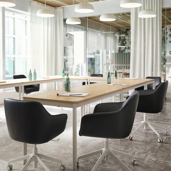 Modern meeting room with TOSSBERG black leather swivel chairs, light wooden table, and white pendant lights.