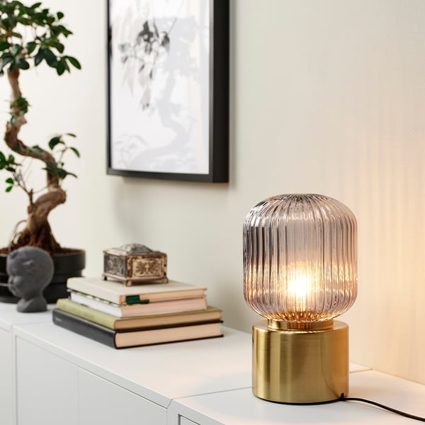 A TRÅDFRI smart led light bulb on a table surrounded by books and a plant.