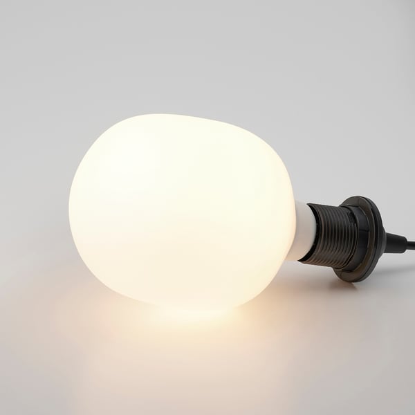 A frosted glass bulb with a black base, lit and glowing softly, emitting a warm, ambient light.