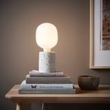 White table lamp on books, gray bowl on wooden table, framed picture.