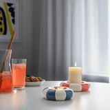 Table setting with tealight holders, drinks, and fruit by window.