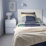 Bedroom with TRATTVIVA bedspread in grey and white on single bed, matching pillowcases, white nightstand with lamp and art.
