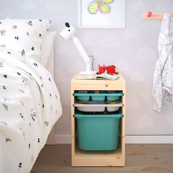 Nightstand TROFAST with teal bins, a lamp, and fox toy next to a patterned bed.