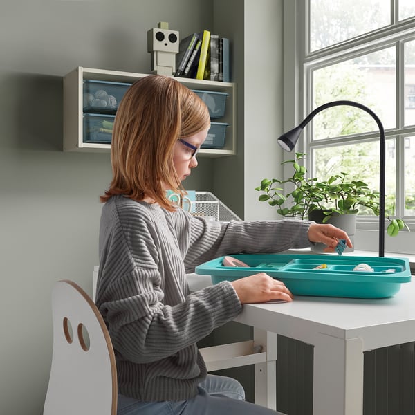 Child organizing tray at white desk with plant and lamp.