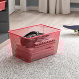 Red mesh storage basket on carpet, containing headphones. Part of TROFAST storage series for organizing items.
