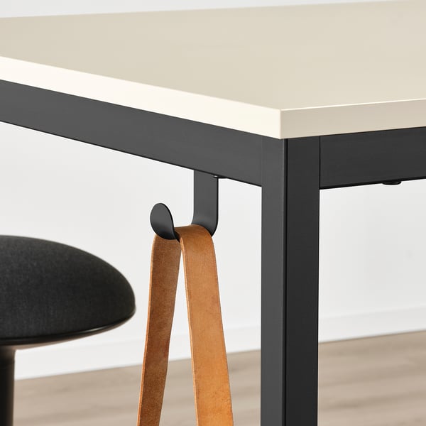 Modern office table with black metal frame, beige top, and hooks for hanging items.
