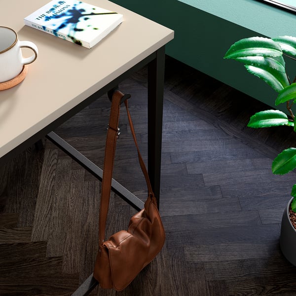 Brown leather bag hangs under desk; white mug, book, and green plant on desk.