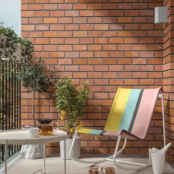 Modern colored rocking chair TUMHOLMEN against brick wall, near plants and table.