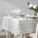 A white dining table set with a black patterned tablecloth, matching plates, glasses, cutlery, and a vase with pink flowers.