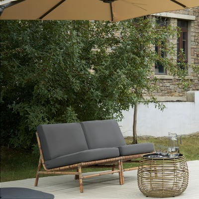 Grey cushioned loveseat with wicker base and table, umbrella.
