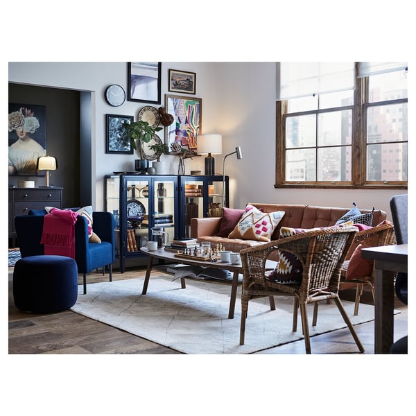 Modern living room with beige rug, brown sofa, wicker chairs, blue accents, city view.