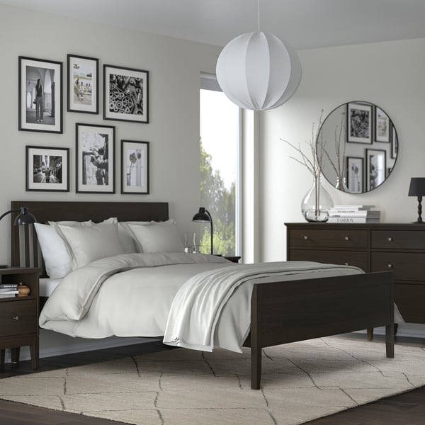 Modern bedroom with TVERSTED rug, dark wood furniture, white bedding, black & white photos, round mirror, and hanging light.