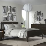 Modern bedroom with TVERSTED rug, dark wood furniture, white bedding, black & white photos, round mirror, and hanging light.