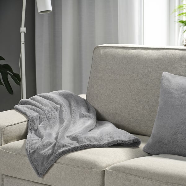 Cozy grey ULLGRIMMIA blanket on light couch, soft & recycled polyester.