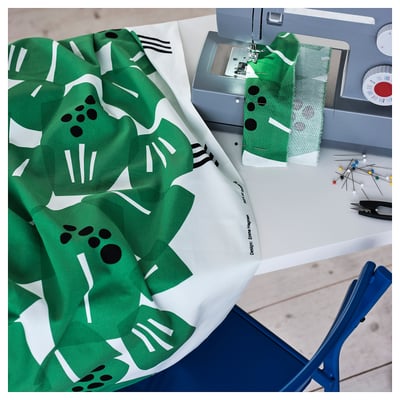 Sewing machine sewing green leaf-patterned fabric on blue table.