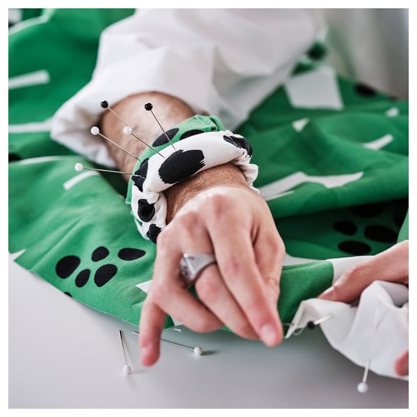 Woman sewing pre-cut fabric with pins at green table.