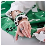Woman sewing pre-cut fabric with pins at green table.