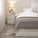 Elegant bedroom with grey wool throw blanket, white bed, and nightstand with lamp.