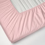 Pale pink fitted sheet with elastic edge, covering white and gray striped mattress.