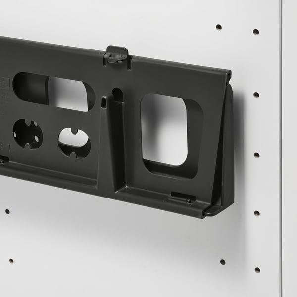 Black plastic storage slider, attached to a white wall, with multiple cutouts and a bungee clip.