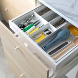 Open kitchen drawer displaying colored utensils, including spatula, spoon, and tongs, arranged in compartments.
